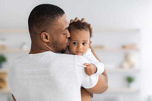 Identifying Pediatric Newborn Hearing Loss Man holding baby against his chest and kissing it on the cheek.